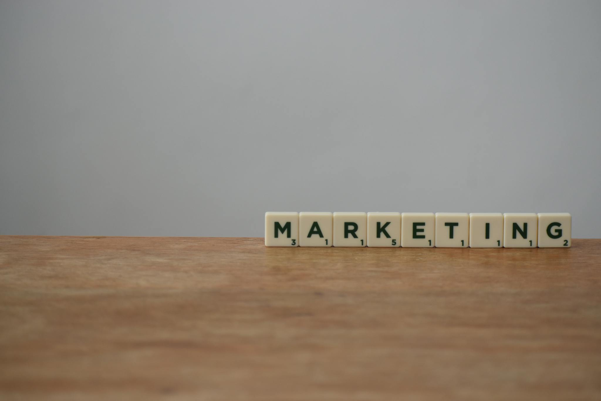 Scrabble tiles spelling 'MARKETING' on a wooden table with a neutral background.